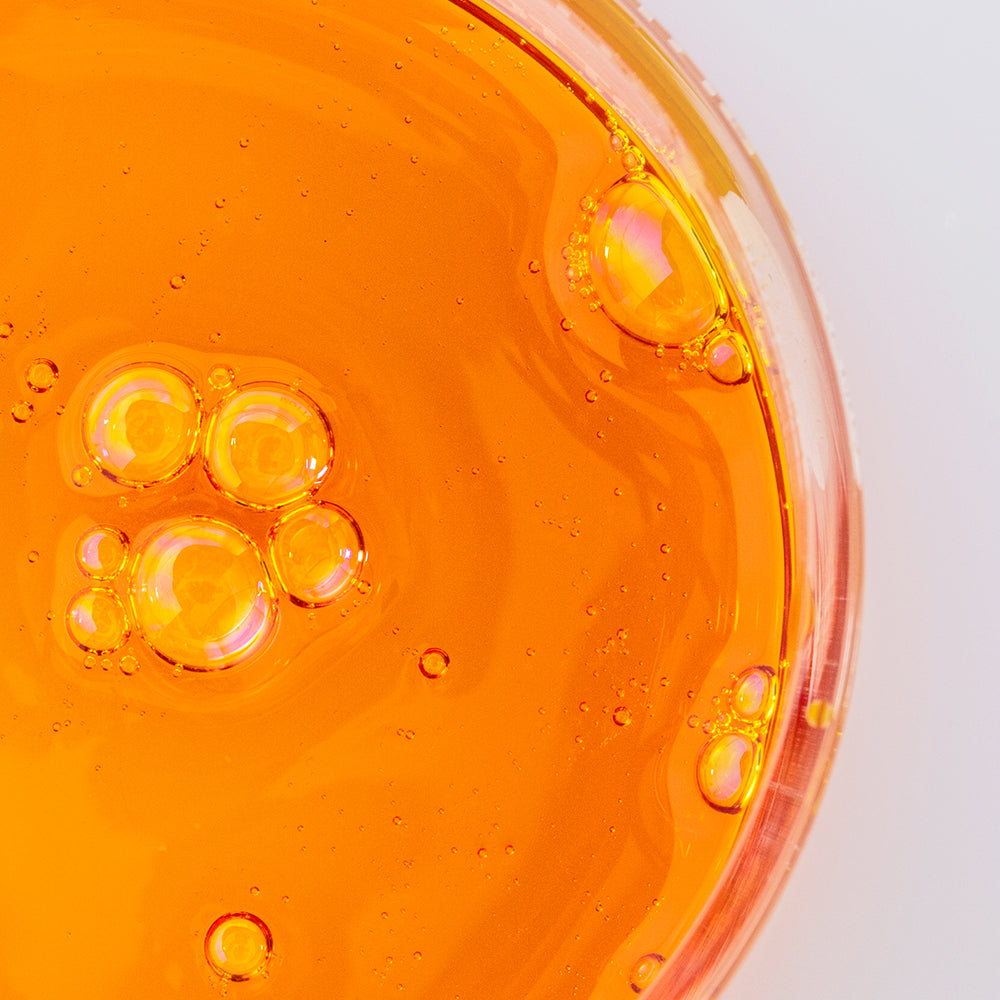 Close-up of orange liquid with bubbles in a transparent container on a white background