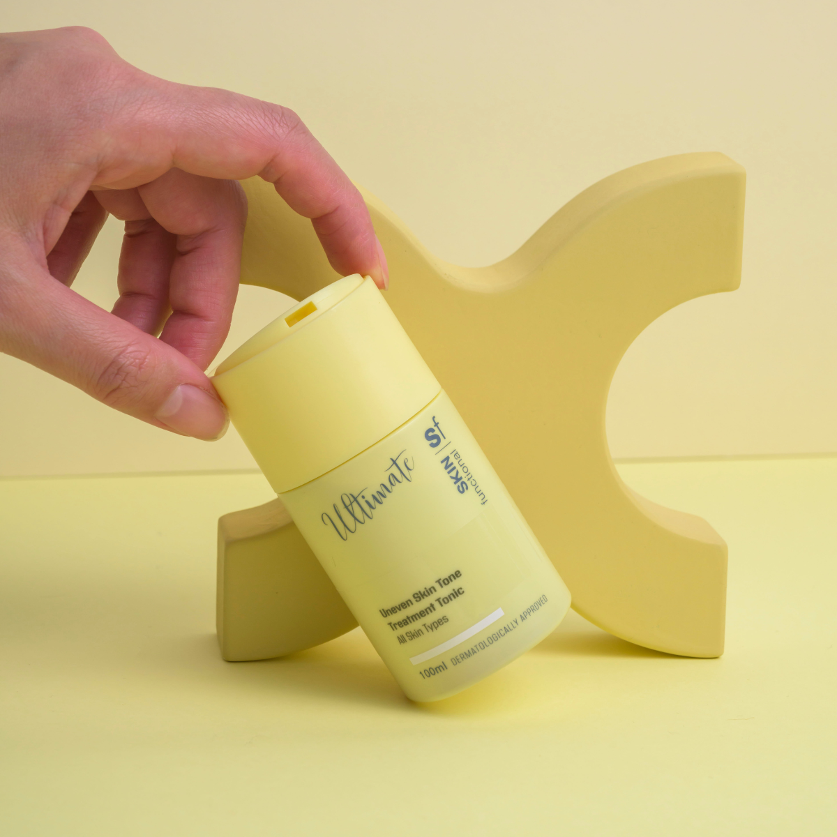 Hand holding a yellow skincare product with a branded label on a yellow background