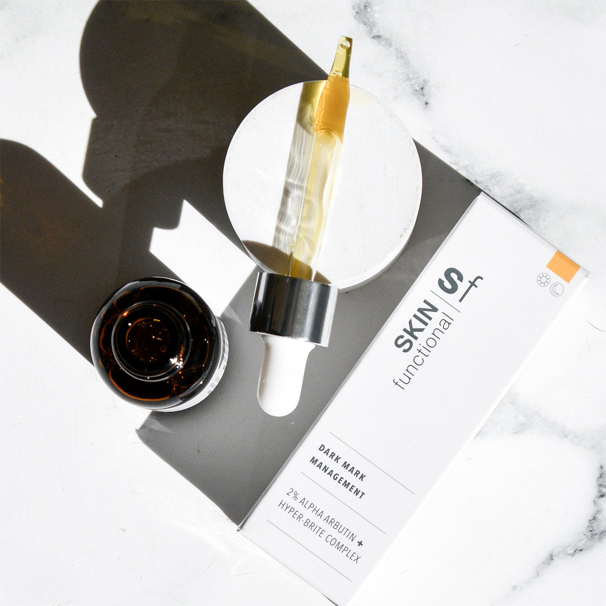 Skin Functional Dark Mark Management product with dropper and jar on a marble surface