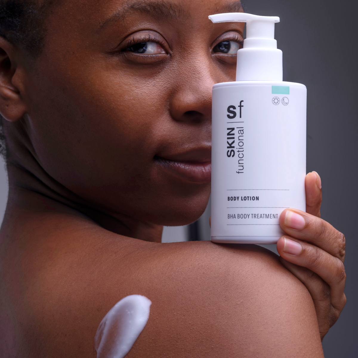 Woman holding a Skin Functional body lotion bottle with visible lotion on her arm.