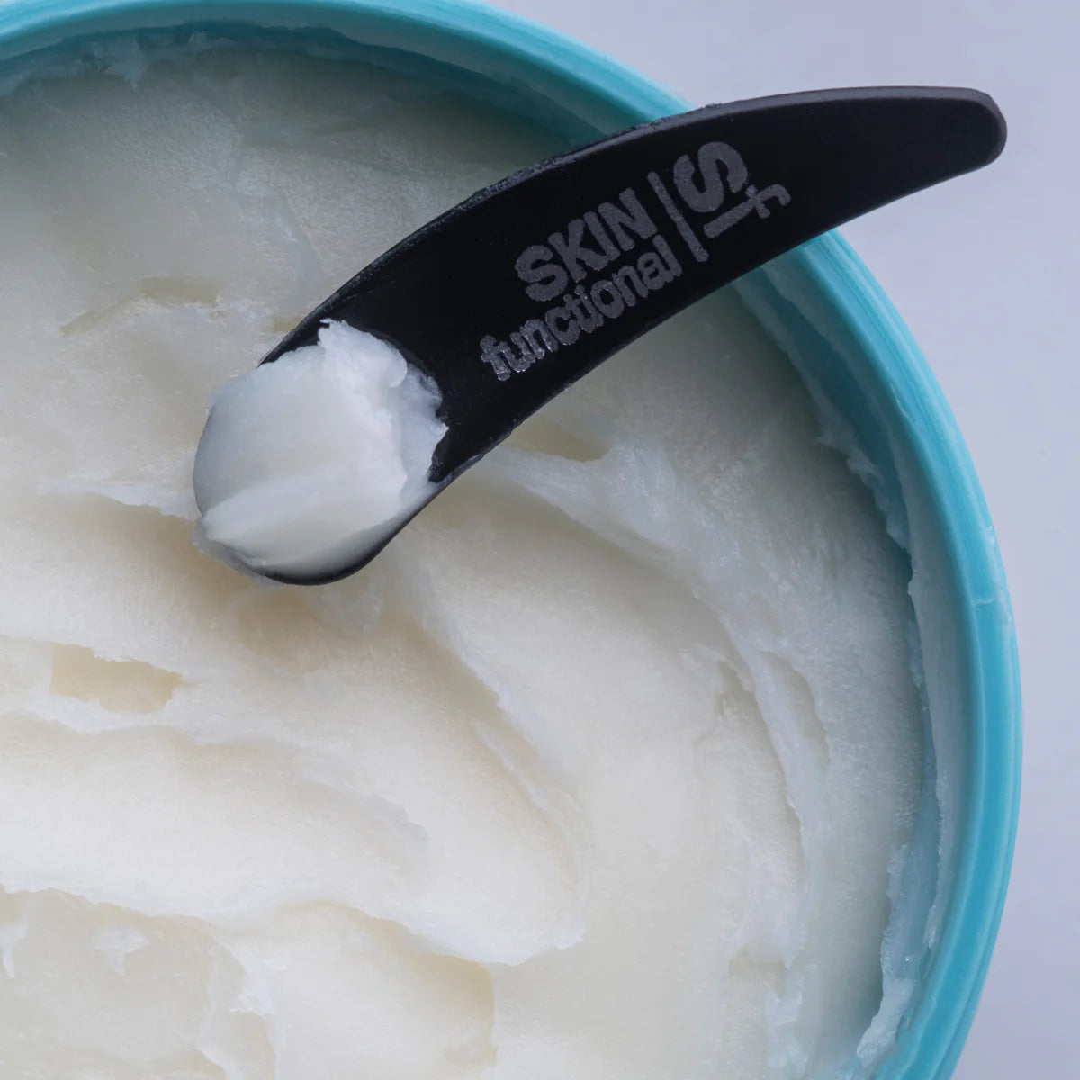 Black spatula with 'Skin Functional' branding on a container of white cream.